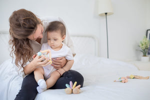 mãe e bebé a brincar com uma Roca Sensorial de Madeira com Chocalho para Bebé